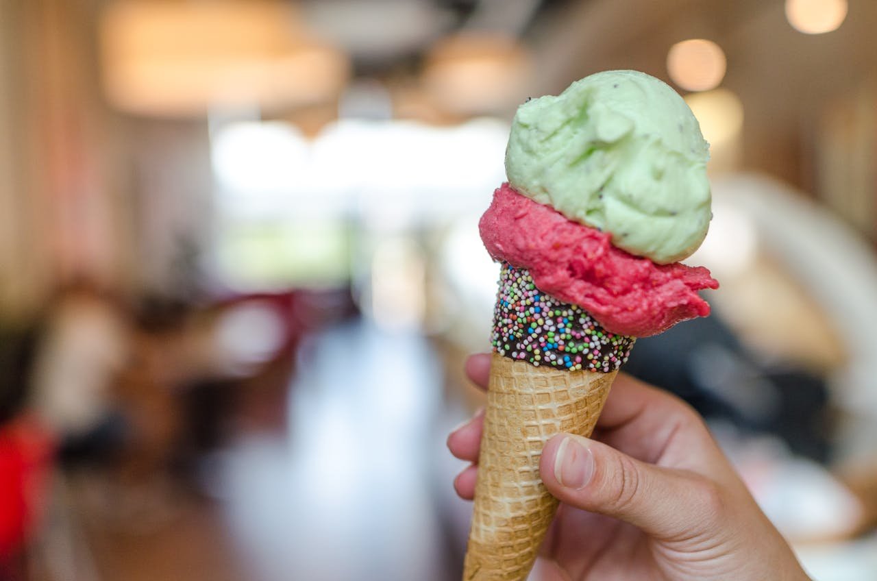 why-choose-us-02 Hand holding a vibrant ice cream cone with sprinkles indoors, perfect summer treat.