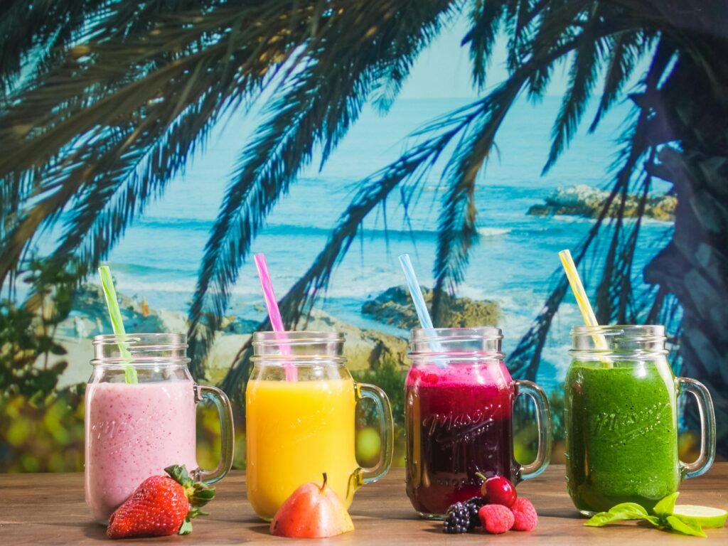 pexels-photo-8181553-8181553 Colorful smoothies in mason jars with a tropical beach backdrop, perfect for summer vibes.